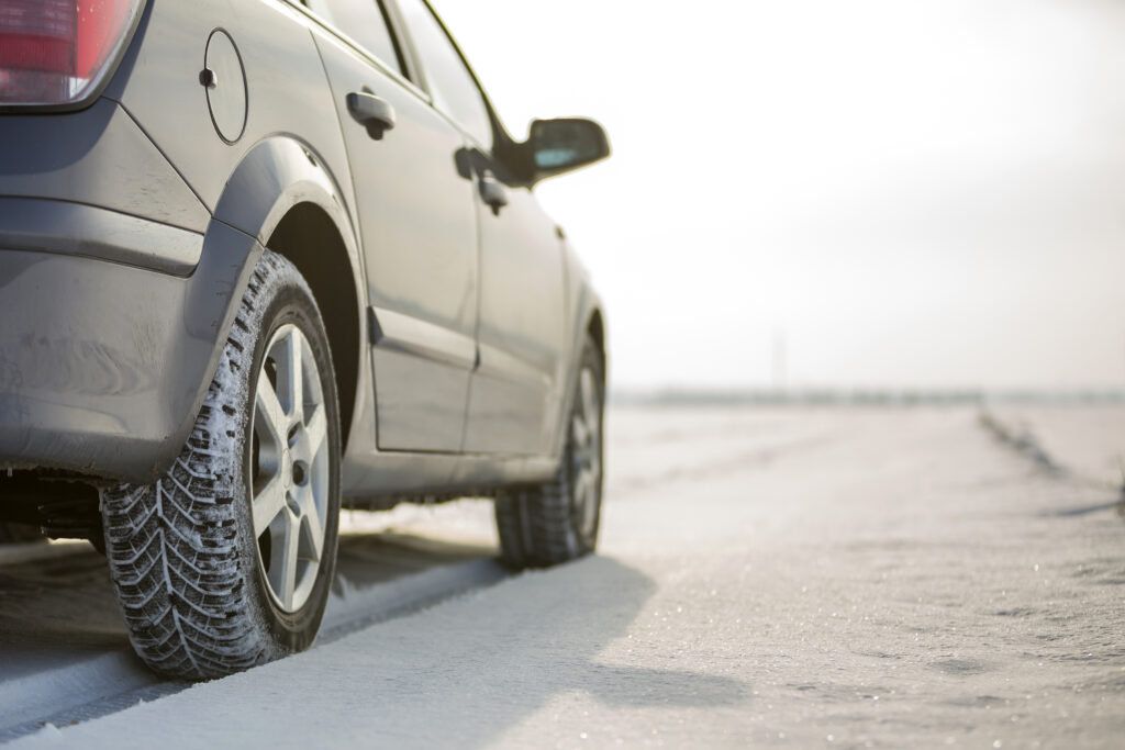 Close up of a car tire parked on snowy road on winter day. Trans